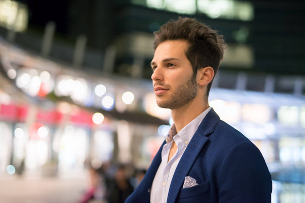Smiling young man walking outdoors in a city at night - Photo, Image