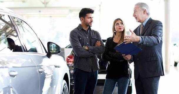 Car dealer explaining a car's features to a couple by reading a document - Zdjęcie, obraz