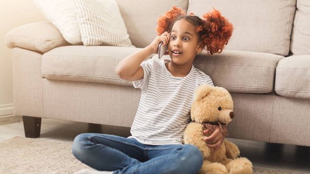 Sürpriz siyah küçük kız yatak odasında telefonda konuşuyor - Fotoğraf, Görsel
