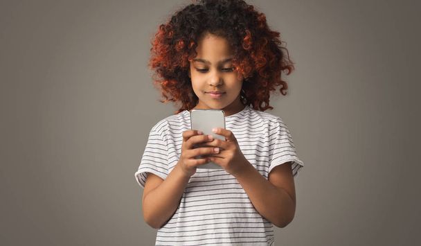 African kid girl playing on smartphone on gray background - Φωτογραφία, εικόνα