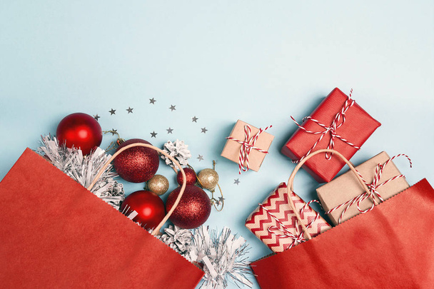 Red shopping bags with christmas decoration and gifts  on a blue background. Holidays shopping and discounts concept. - 写真・画像