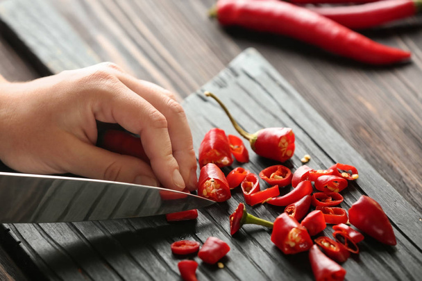 Woman cutting fresh chili peppers on wooden board, closeup - Photo, Image