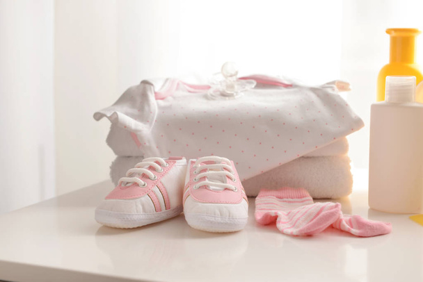 Ropa de bebé, zapatos y cosméticos en la mesa
 - Foto, imagen