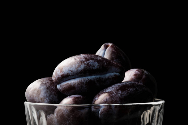 Fresh blue plums in a glass bowl isolated on a black background - Fotografie, Obrázek