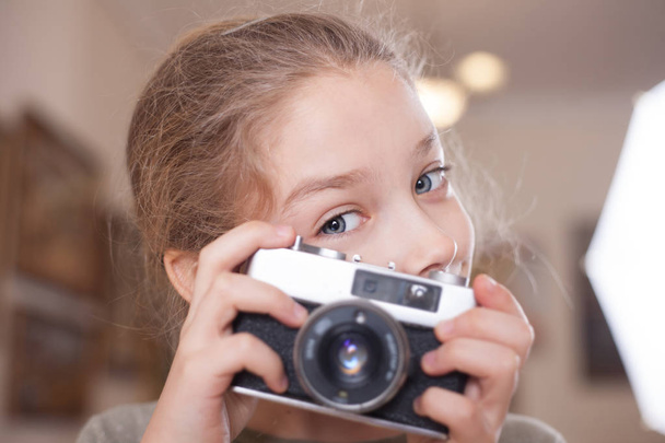 Girl with a retro camera makes a photo, studio shot. - Фото, зображення