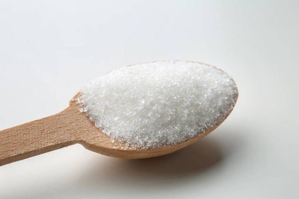 Rakeistettu sokeri puisessa lusikassa valkoisella pohjalla
 - Valokuva, kuva