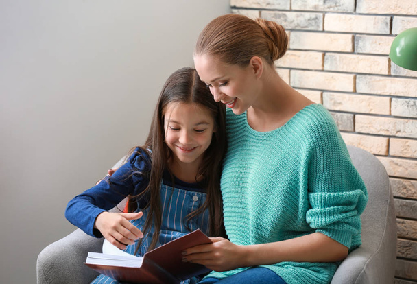 Linda chica con madre leyendo libro en casa
 - Foto, imagen