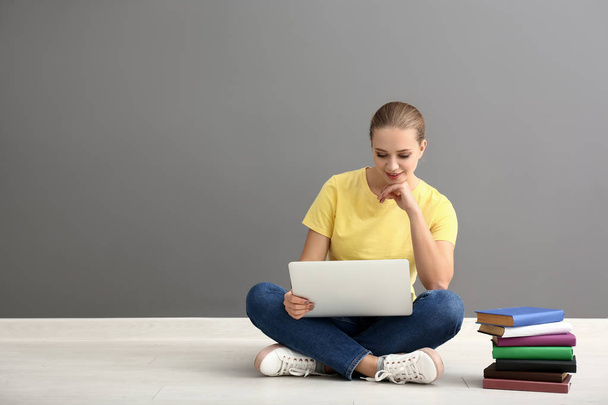 Female student with laptop sitting near grey wall - Foto, Imagem