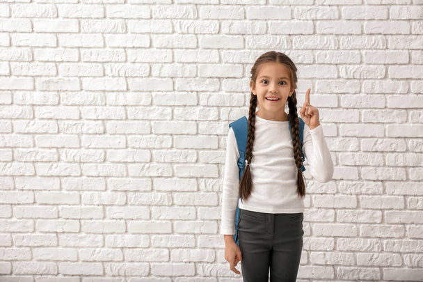 Милая девушка с рюкзаком и поднятым пальцем на белом кирпичном фоне
 - Фото, изображение