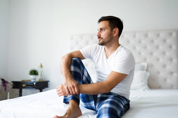 Portrait of young unhappy man sitting on bed - Фото, зображення