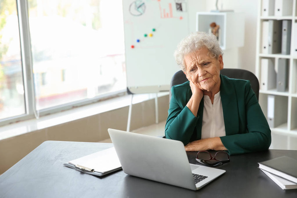 Senior vrouw lijdt aan nekpijn zittend aan tafel met laptop - Foto, afbeelding