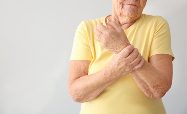 Senior woman suffering from pain in wrist on light background - Photo, Image