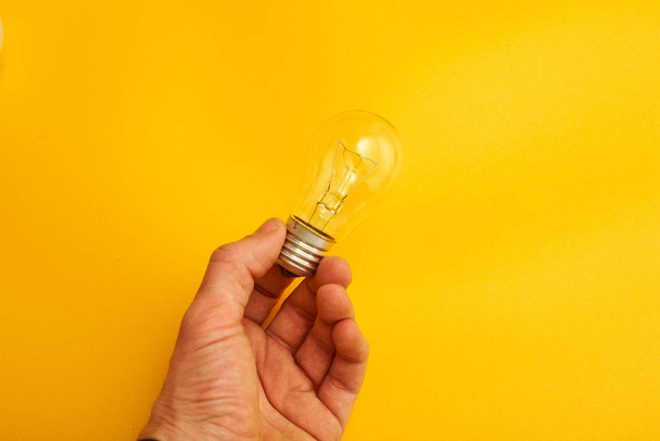 hand holding light bulb on yellow background - Foto, afbeelding