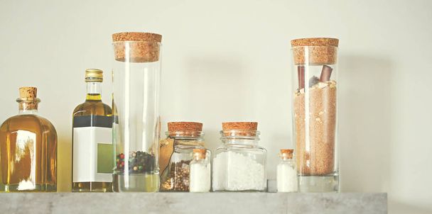 Selective focus of arranged jars with various spices and olive oil on kitchen shelf. Toned photo - Foto, immagini