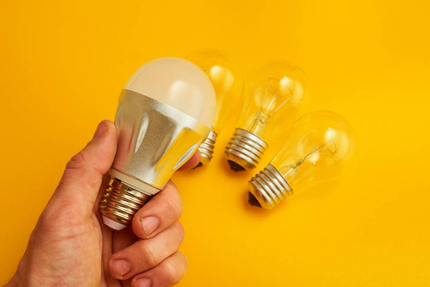 hand holding light bulb on yellow background - Zdjęcie, obraz
