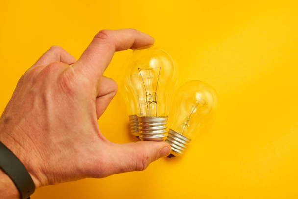 hand holding light bulb on yellow background - Zdjęcie, obraz