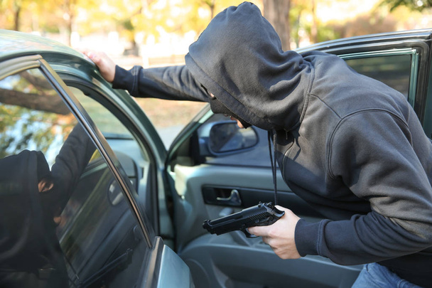 Мужчина-вор с пистолетом возле открытой машины
 - Фото, изображение