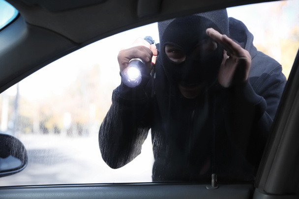 Ladrón masculino con linterna mirando dentro del coche
 - Foto, imagen
