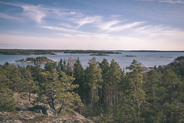 rocky coastline in Finland with few pine trees and calm water in summer - vintage retro look - 写真・画像