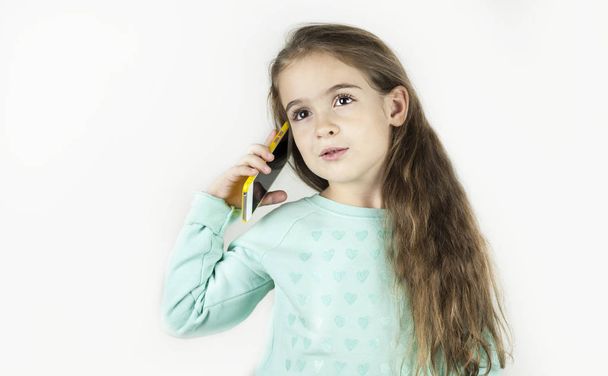 Bright beautiful little girl in headphones with the phone is emotionally surprised on an isolated background. - Foto, immagini