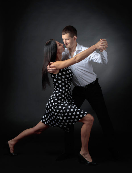 Young beautiful woman in polka dot dress and man in white shirt dancing tango. Couple in love dancing in the Studio. - Photo, image