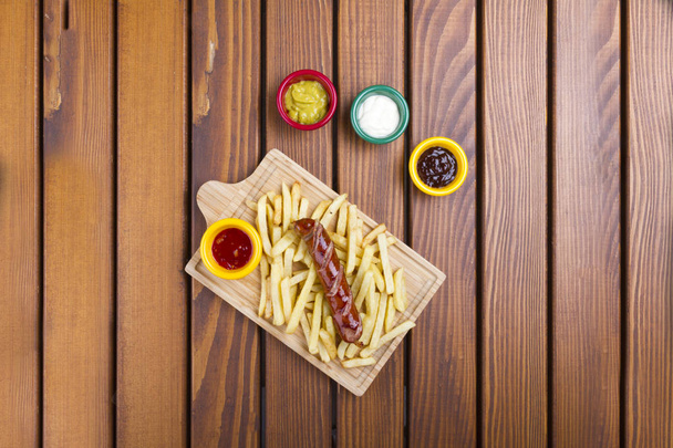 Vista superior da salsicha grelhada de carne de porco frankfurter com batatas fritas, batatas fritas e molhos de mergulho
. - Foto, Imagem
