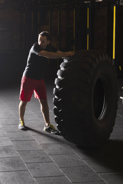 Black shirt man flipping big heavy tire at the gym. - Fotó, kép