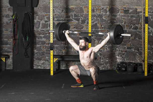 Young bearded and shirtless athlete training with a heavy barbell at the gym. Dark photography concept with copy space area. - Photo, Image