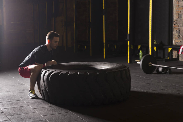 Černá košile muž překlápění velké těžké pneumatiky v tělocvičně. - Fotografie, Obrázek