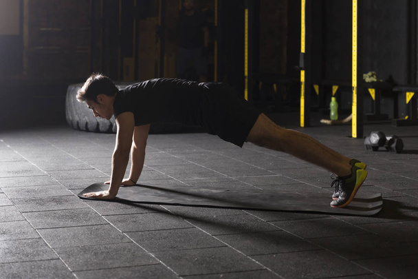 Νεαρός αθλητής με μαύρα ρούχα εξάσκηση push ups στο γυμναστήριο. - Φωτογραφία, εικόνα