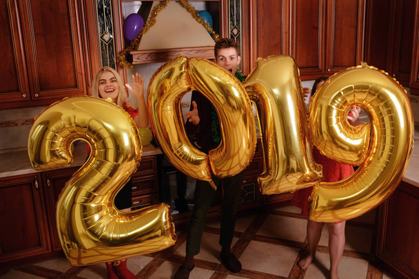Nouvel an 2019 arrive. Groupe de jeunes gens joyeux portant des numéros de couleur or et amusez-vous à la fête
. - Photo, image