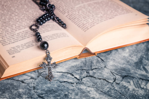 Black rosary and cross on the Bible on a gray table. Religion at school. - Fotoğraf, Görsel