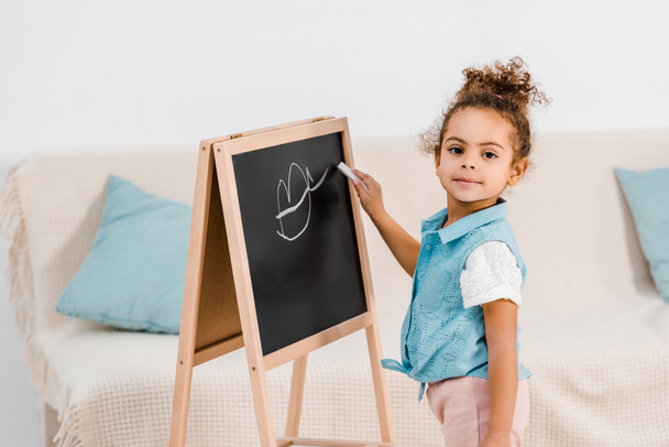 cute african american child drawing on chalkboard and looking at camera - Fotoğraf, Görsel