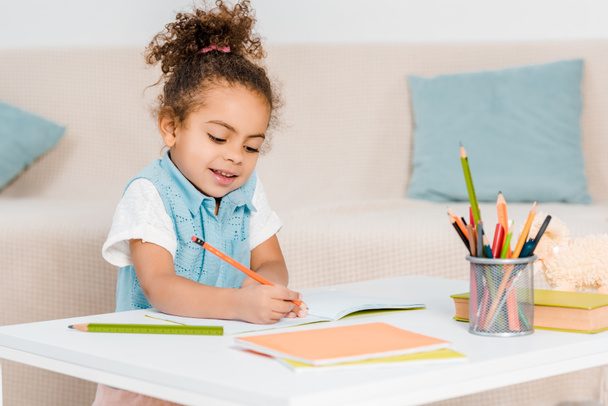 adorable smiling african american child studying and writing with pencil - Foto, imagen