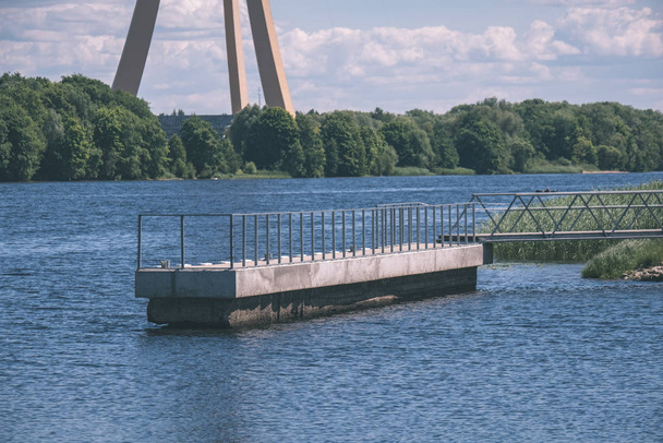 деревянный и композитный материал пешеходный мост через воду в зеленой летней лесной местности с озером
 - Фото, изображение