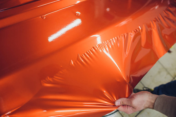 Car wrapping specialist putting vinyl foil or film on car wrapping protective film yacht, boat, ship, car, mobile home. orange film hand pulls - Foto, Imagem