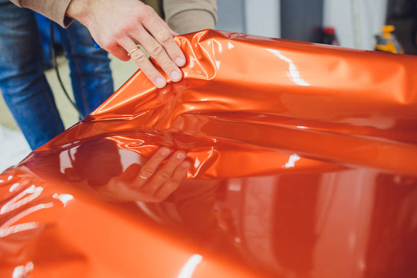 Car wrapping specialist putting vinyl foil or film on car wrapping protective film yacht, boat, ship, car, mobile home. orange film hand pulls - Zdjęcie, obraz