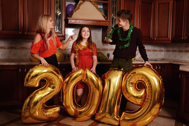 Nouvel an 2019 arrive. Groupe de jeunes gens joyeux portant des numéros de couleur or et amusez-vous à la fête
. - Photo, image