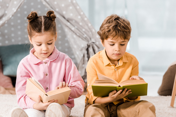 entzückende Kinder sitzen auf Teppich und lesen gemeinsam Bücher   - Foto, Bild