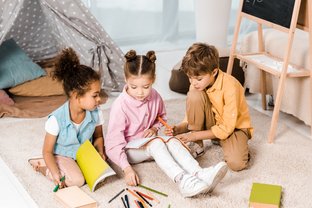 high angle view of adorable multiethnic children sitting on carpet and studying together    - Photo, Image