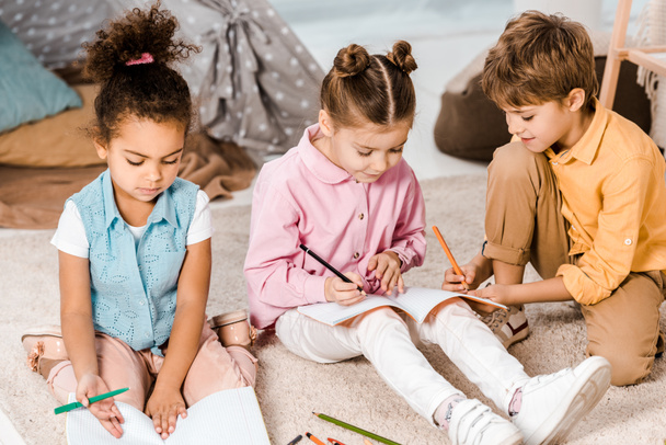adorable multiethnic children sitting on carpet and studying together   - Foto, Bild