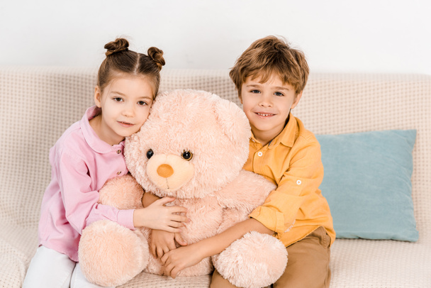 adorable happy kids hugging pink teddy bear and smiling at camera - Fotó, kép