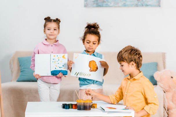 lindos niños multiétnicos sosteniendo cuadros y pintando juntos
 - Foto, Imagen