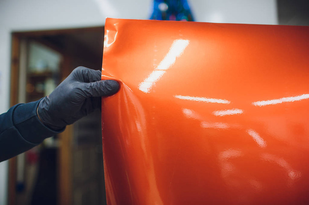 Car wrapping specialist putting vinyl foil or film on car wrapping protective film yacht, boat, ship, car, mobile home. orange film hand pulls - Foto, Imagen