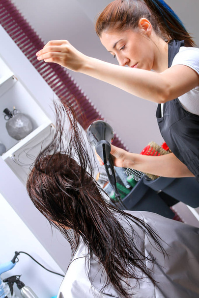 Girl in beauty salon while an hair stylist dry her hair - Photo, Image