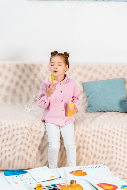 adorable child sitting on couch and blowing soap bubbles - Photo, Image