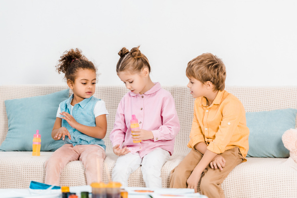 adorable multiethnic children sitting on sofa and playing with soap bubbles     - Fotó, kép