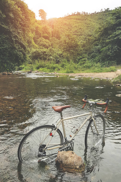 レンズで太陽のフレアと川にビンテージ冒険自転車立って - 写真・画像