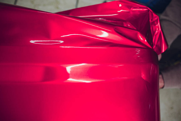 Car wrapping specialist putting vinyl foil or film on car wrapping protective film yacht, boat, ship, car, mobile home. pink red film hand pulls - 写真・画像
