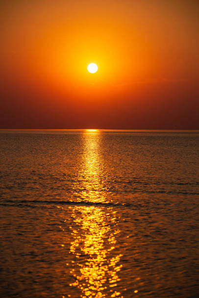 ярко-красный оранжевый закат над спокойным морем летом с солнечным способом отражения в воде
 - Фото, изображение